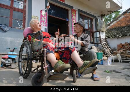 NANCHANG, 8. September 2021 (Xinhua) -- Luo Anmin spricht mit seiner Frau im Hof des Dorfes Xuluo im Bezirk Nanchang, Provinz Jiangxi, Ostchina, 5. September 2021. Luo Anmin ist 76 Jahre alt. 2008 litt seine Frau Wan Zhaolian an Hirntumor und verlor leider das Bewusstsein, aber Luo gab nie auf. Er sprach mit seiner Frau und gab ihr jeden Tag Massagen, in der Hoffnung, dass es ihr eines Tages besser gehen könnte. Nach drei Jahren liebevoller Fürsorge geschah das Wunder. 2011 erlangte Wan Zhaolian wieder das Bewusstsein, was Luo mehr Hoffnung gab, obwohl sie immer noch nicht sprechen und gehen konnte. Luo sagte, er liebe es Stockfoto