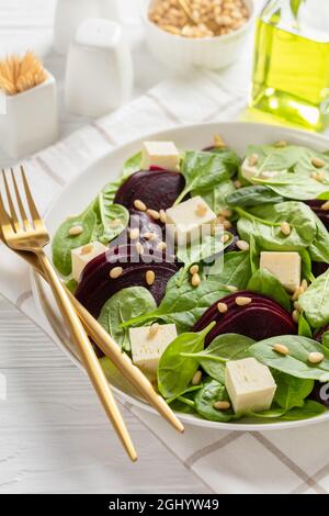 Gerösteter Rübensalat mit gewürfeltem Feta-Käse, Pinienkernen und Spinat auf einem weißen Teller mit goldenem Besteck auf einem Holztisch, kanadische Küche, vertikale VI Stockfoto