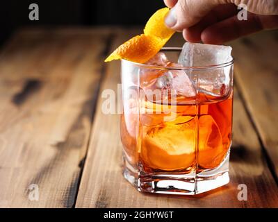 Ein Mann legt eine Orangenschale auf einen Felsen. Negnoni-Cocktail. Speicherplatz kopieren. Stockfoto