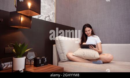 Stay Home Concept ein Mädchen mit dem weißen T-Shirt sitzt auf dem gemütlichen großen Sofa im schön dekorierten Wohnzimmer. Stockfoto