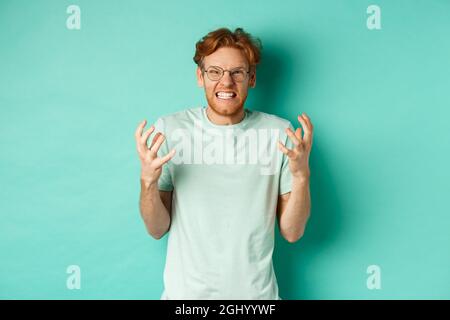 Porträt von verzweifelten und wütenden Rotschopf Kerl verlieren Temperament, schreien und Händeschütteln empört, starrte mit wütendem Gesicht auf die Kamera, stehen über Stockfoto