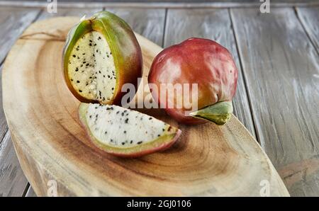 Peruanische Apfelkaktus Früchte ganz und auf Holzständer auf grauem Brett geschnitten. Wissenschaftlicher Name Cereus repandus. Stockfoto