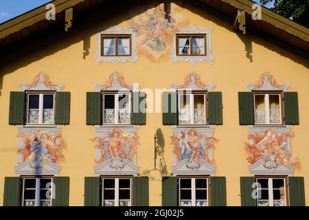 Schöne Fresken an der Gebäudefassade mit Fenstern, Fensterläden und Vorhängen kurz vor Sonnenuntergang in Oberammergau, Bayern, Deutschland Stockfoto