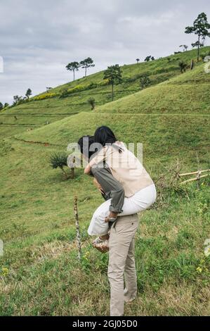 Romantische junge asiatische Paar Huckepack Fahrt auf der Weide Hügel in der Landschaft im Urlaub Stockfoto