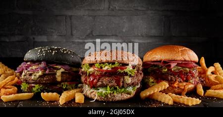 Köstliche verschiedene Hamburger mit bunten Brötchen und Koteletts serviert mit Pommes auf dem Tisch auf dunklem Hintergrund Stockfoto