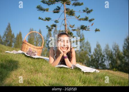 Glückliche junge asiatische Frau, die sich ausruhte und lächelte und am Wochenende ein Picknick auf dem Gras hatte Stockfoto