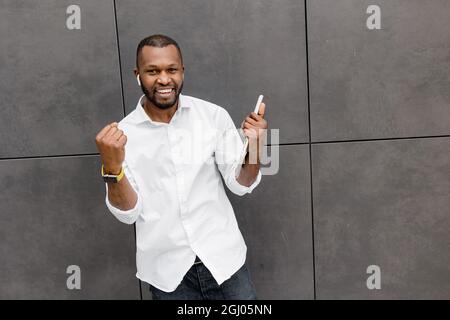 Ein aufgeregter, stilvoller Geschäftsmann freut sich über die Arbeitsförderung, lächelt und blickt auf die Kamera. Überglücklich männliche Studenten oder Angestellte erhielten großartige Neuigkeiten Stockfoto