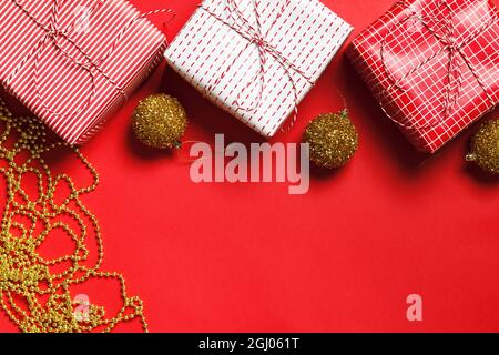 Weihnachtskomposition. Geschenkboxen, goldene Weihnachtskugeln und Perlen auf rotem Hintergrund. Flach liegend, Draufsicht, Kopierbereich Stockfoto