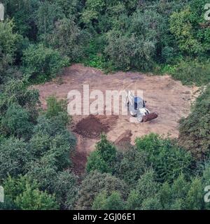 Der Bagger bereitet den Boden auf dem Feld im Wald unter den Bäumen für die Landschaftsgestaltung und Landwirtschaft, Draufsicht Stockfoto