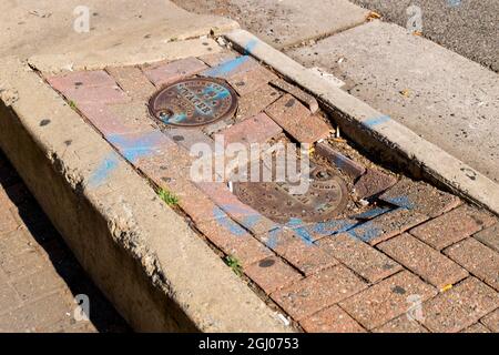 Zwei Stahlschachtabdeckungen, die auf einem gemauerten Median eingekalten sind und repariert werden müssen. In Arlington, Virginia. Stockfoto