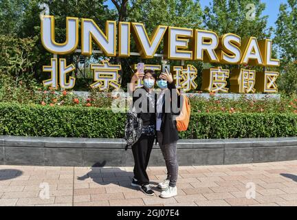 Touristen mit Gesichtsmasken posieren für ein Selfie vor den chinesischen und englischen Schildern des universellen Pekinger Resorts. Universal Beijing Resort ist ein weit verbreitetes Themenpark-Ziel mit mehreren neuen Attraktionen zusammen mit den besten Universal-Fahrgeschäften, Shows und Attraktionen aus der ganzen Welt, die speziell für das kulturelle Erbe Chinas entwickelt wurden. Universal Parks & Resorts, eine Einheit von Comcast NBCUniversal, bietet Gästen auf der ganzen Welt ein immersives Themenerlebnis. Universal's Themenparks sind bekannt für immersive Erlebnisse mit hohem Th Stockfoto