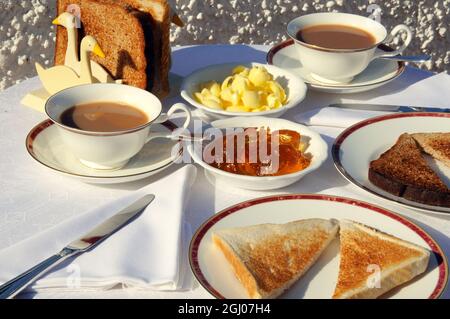 Scheiben brauner und weißer Toast mit einer Begleitung von Orangenmarmelade, weicher Milchbutter und zwei Tassen Tee. Stockfoto