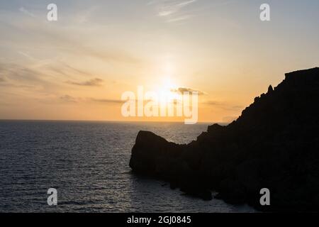 Sonnenuntergang an einem schönen Frühlingstag, von Anchor Bay, Mellieha, Malta aus gesehen. Die Sonne untergeht über dem Horizont mit einigen Wolken und ruhigen Meer. Stockfoto