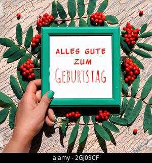 Deutscher Text alles gute zum Geburtstag bedeutet Alles Gute zum Geburtstag. Natürliche Herbstdekorationen. Orangefarbene Eberesche mit Blättern auf hellbeige strukturiertem Holz Stockfoto