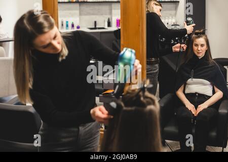 Friseurmeisterin trocknet die Haare des Mädchens nach dem Waschen in einem Schönheitssalon mit einem Haartrockner. Stockfoto