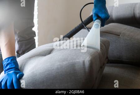 Reinigungsservice. Mann Hausmeister in Handschuhen und einheitliche Vakuum-saubere Sofa mit professioneller Ausrüstung Stockfoto