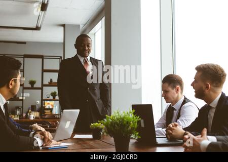 Ein Team junger Geschäftsleute in Anzügen, die in einem Büro zusammenarbeiten und miteinander kommunizieren. Geschäftsleute und Manager in einem Meeting. Stockfoto