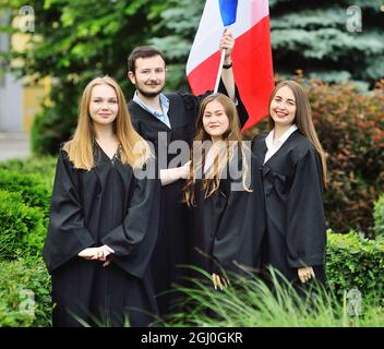 Gruppe von Studenten Absolventen der Fakultät für Fremdsprachen in Roben halten die Flagge Frankreichs in ihren Händen Stockfoto