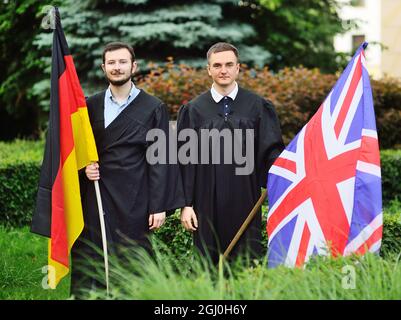 Zwei junge Studenten der Fakultät für Fremdsprachen in Gewändern halten die Fahnen Deutschlands und Großbritanniens in den Händen Stockfoto