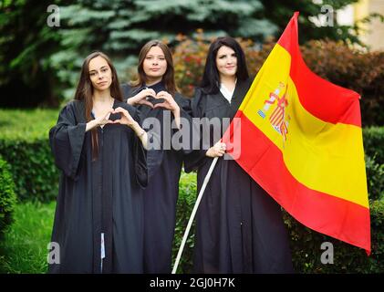 Gruppe von Studenten Absolventen der Fakultät für Fremdsprachen in Roben halten die Flagge Spaniens in den Händen Stockfoto