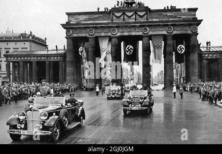 Olympische Spiele 1936, Berlin - Adolf Hitler führt in einem offenen Wagen eine Flotte von Autos durch das Brandenburger Tor, vorbei an Zuschauern auf dem Weg zu den Olympischen Spielen 1936. (Der Führer Adolf Hitler, schirmherr der Olympischen Spiele, gibt solche durch das Spalier der begehrten Volksenge zum Reichssportfeld, um die Spiele feiern zu eröffnen) ©TopFoto Stockfoto