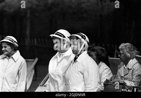 Zwei weiß gekleidete Frauen tragen Hutbänder unter ihren Chins, um zu verhindern, dass sie fallen, bei den Amateur National Championships der English Women's Bowling Association im Wimbledon Park, London, England. 25. August 1969 Stockfoto