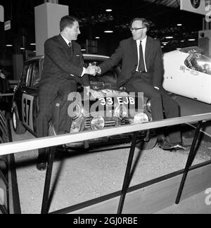 London: Paddy Hopkirk (links) und sein Beifahrer Henry Liddon (rechts) schütteln sich die Hände über ihren Morris Cooper, als ihr Auto heute auf der Racing Car Show in Olympia in London auf einem Sonderstand fuhr. Die beiden flogen gestern nach dem Sieg bei der Rallye Monte Carlo 1964 ein, der ersten Briten seit dem 1950 27. Januar 1964 Stockfoto