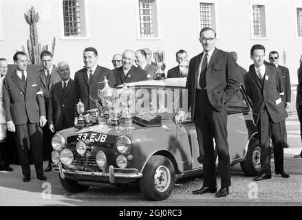 Monte Carlo, Monaco: Die Haube des Morris Cooper S ist mit Trophäen bedeckt, der britische Paddy Hopkirk (vierter von links) und der Beifahrer Henry Liddon (Vordergrund) sind nach der Präsentation der Trophäen hier am 25. Januar 1964, am Ende der Rallye Montre carlo 1964, abgebildet. Paddy ist der erste britische Fahrer, der die Rallye seit 1956 gewonnen hat. Die British Motor Corporation ( BMC ) gewann den Herstellerpreis am 27. Januar 1964 Stockfoto