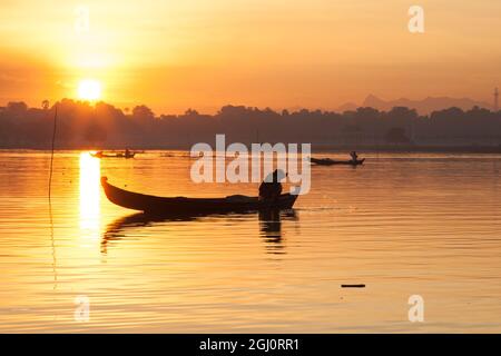 Sonnenaufgang über dem See mit Fischern auf Booten, die im See in der Nähe einer hölzernen Fußgängerbrücke fischen. U Bein Brücke über den Taungthaman See in der Nähe von Amarapura i Stockfoto