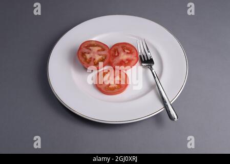 Eine in Scheiben geschnittene Tomate auf einem weißen Porzellanteller mit einer Gabel Stockfoto