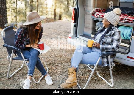 Multirassische Freundinnen, die Spaß beim Campen mit dem Wohnmobil haben, während sie Kaffee im Freien trinken - Fokus auf ältere afrikanische Frau Gesicht Stockfoto