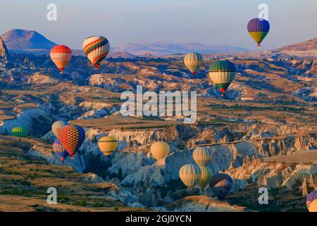 Türkei, Anatolien, Kappadokien, Goreme. Heißluftballons fliegen über/zwischen Felsformationen und Feldlandschaften im Red Valley, Goreme National Park, Stockfoto