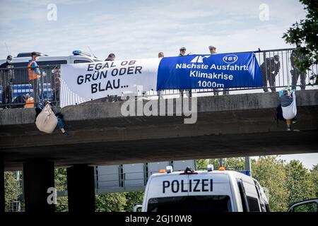 Banner: 'Nächste Abfahrt: Klimakrise 1000m', egal ob GRÜN ODER BLAU. Anlässlich der Eröffnung der Automobilausstellung (IAA) in München wurde am 07.09.2021 die A94 kurz vor der Ausfahrt zum Messegelände die Autobahn A94 mittels einer abseilen-Aktion von Klimaaktivist*innen blockiert. You have receive to Green washing in the Autoindustry. * Banner Eading: " regardless ob blau oder grün . Nächster Ausgang Klimakrise 1000m '. Am 7. September 2021 wurde die Ausfahrt zur Messe der Autobahn A94 von Klimagerechtigkeitsaktivisten blockiert. Die A94 bringt Autofahrer zum Inte Stockfoto