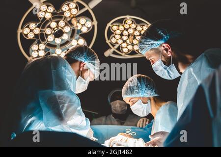 Ein internationales Ärzteteam führt eine komplexe chirurgische Operation an einem unter Anästhesie stehenden Patienten durch. Moderner Operationssaal und erfahrene Chirurgen Stockfoto