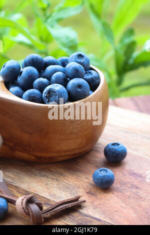 Heidelbeeren in einem Holzbecher auf einem Holztisch im Freien Stockfoto