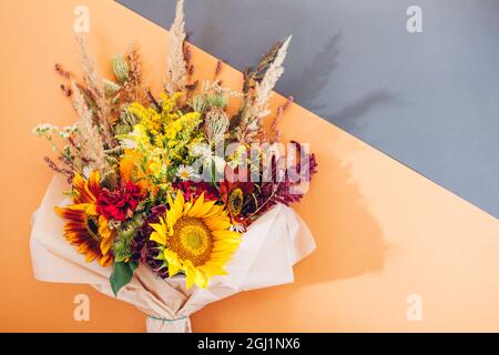 Herbststrauß aus gelb-rot-orangen Blumen, eingewickelt in Papier und auf dem Hintergrund angeordnet. Sonnenblumen, Zinnien und Gräser Stockfoto