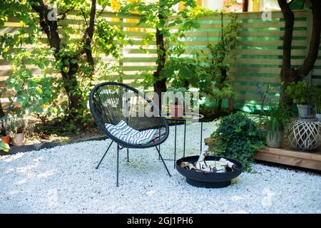 Veranda des Hauses mit Sessel, Couchtisch und Pflanztöpfen. Metallschale mit schwarzem Kamin im Garten auf der Terrasse im Hinterhof. Terrassenmöbel im Freien Stockfoto