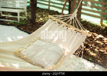 Weiße Hängematte und Kissen für Entspannung im Garten Schatten im Garten an einem Sommernachmittag. Komfortable Hängematte im Boho-Stil mit Kissen am Baum. Stockfoto