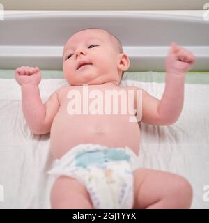 Der kleine Junge liegt in einer Windel auf dem Wickeltisch in der Klinik. Glückliches Kind beim Wechseln der Kleidung auf Windel vor dem Termin mit dem Arzt in der Zusammenarbeit Stockfoto