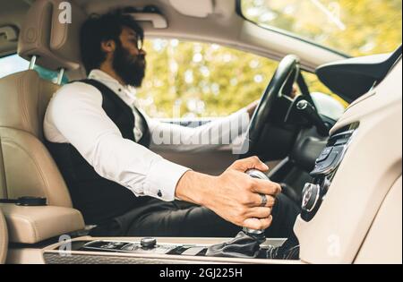 Stilvoller gutaussehender Hindu-Geschäftsmann mit Brille und Bart arbeitet auf dem Rücksitz des Autos und nutzt das Telefon. Sichere und komfortable Luxusreisen Stockfoto