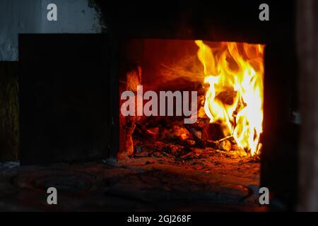 Unschärfe-Effekte im Hintergrund der Feuerflamme. Brennendes Brennholz im alten Ofen oder Ofen. Dunkel und schwarz. Orangefarbene Flamme. Wärmeenergie. Öffnen Sie die Eisentür. Rustikales Haus. Lodernd Stockfoto