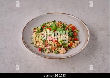 Nahaufnahme des Tabbouleh-Salats. Traditionelles nahöstliches oder arabisches Gericht mit Petersilie, Minze, Bulgur und Tomaten in einer Schüssel auf hellem Hintergrund Stockfoto