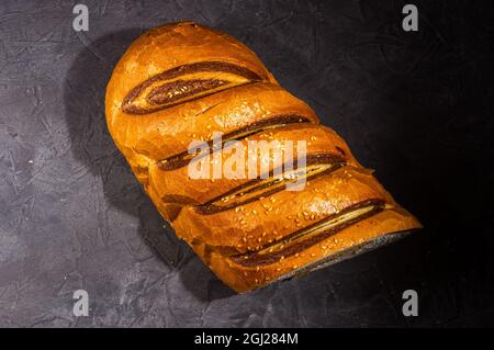Ungewöhnlicher, frischer zweifarbiger Laib Brot auf schwarzem Hintergrund, Foto in einem niedrigen Ton bei hartem Licht, Nahaufnahme. Stockfoto