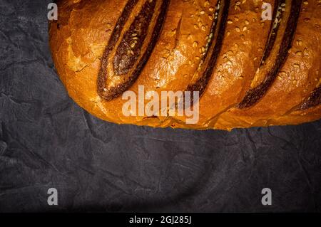 Ungewöhnlicher, frischer zweifarbiger Laib Brot auf schwarzem Hintergrund, Foto in einem niedrigen Ton bei hartem Licht, Nahaufnahme. Stockfoto