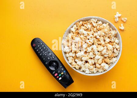 Schüssel Popcorn und TV-Fernbedienung auf gelbem Hintergrund, Draufsicht mit Kopierplatz. Freizeit- und Home-Entertainment-Konzept Stockfoto