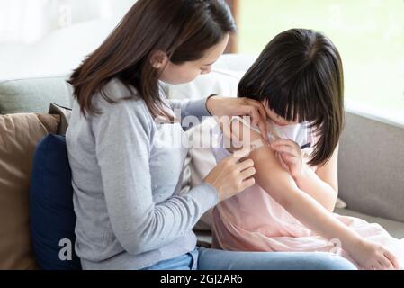 Asiatische Mutter, die ihre Tochter zu Hause mit einem Pflaster-Haftverband aufklebt Stockfoto