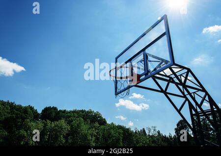 Basketballkorb und transparentes Glas-Backboard vor blauem Himmel im Stadtpark an sonnigen Tagen. Straßensportgeräte. Speicherplatz kopieren Stockfoto