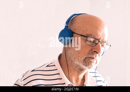 Porträt eines alten Mannes nachdenklich mit Kopfhörern mit weißem Hintergrund, isoliert mit Copyspace. Stockfoto