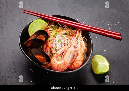 Wok mit gebratenen Nudeln, Garnelen und Gemüse auf Steingrund Stockfoto