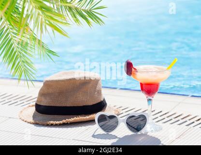 Tropisches Cocktailglas, Sonnenhut und herzförmige Sonnenbrille am Rand des Swimmingpools. Mit Kopierbereich Stockfoto